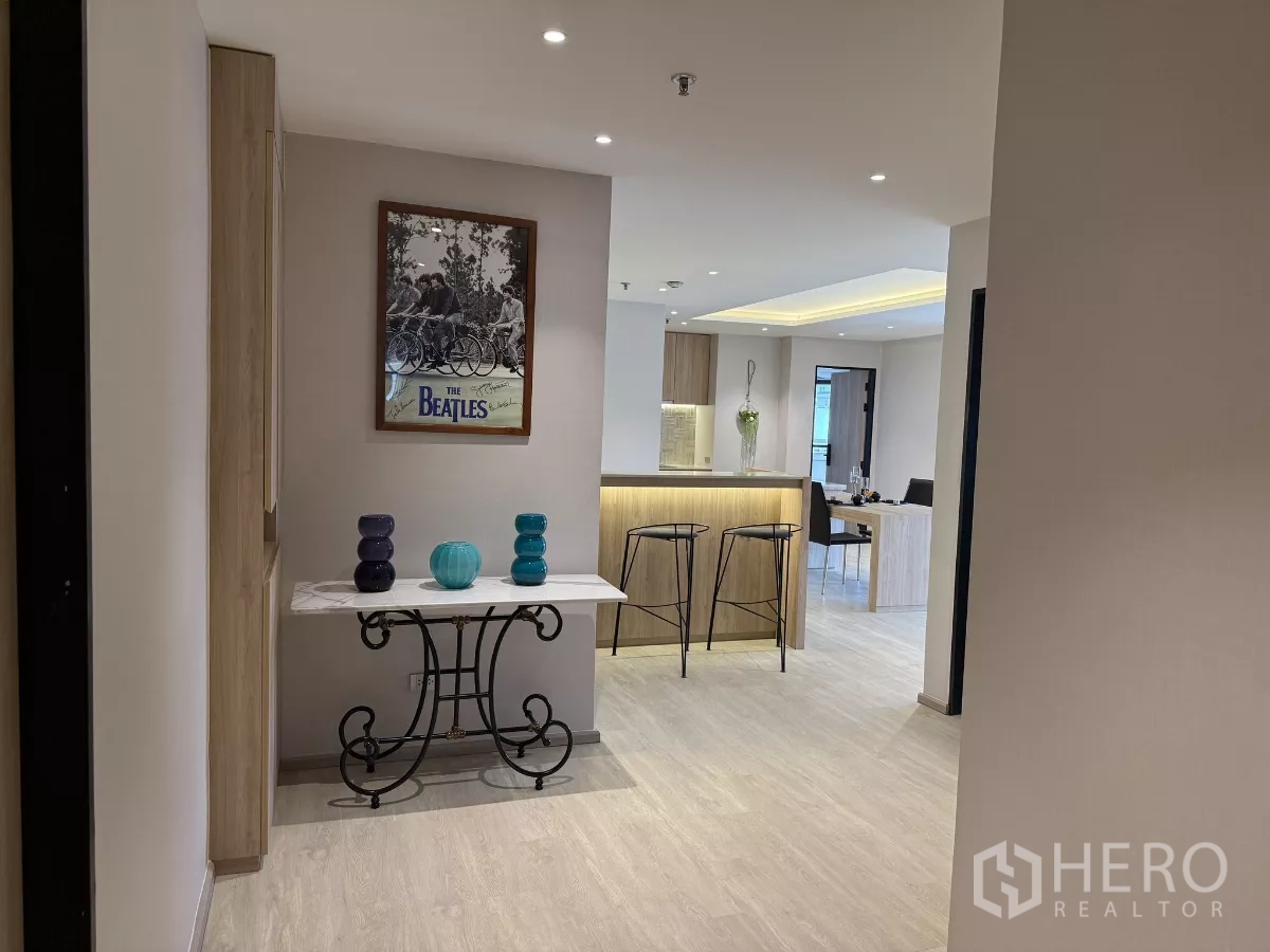 คอนโด ให้เช่าในWatthana, Bangkok - โถงทางเข้าพร้อมโต๊ะคอนโซลและของตกแต่ง มองไปยังเคาน์เตอร์บาร์ครัวไม้พร้อมสตูลสองตัว.