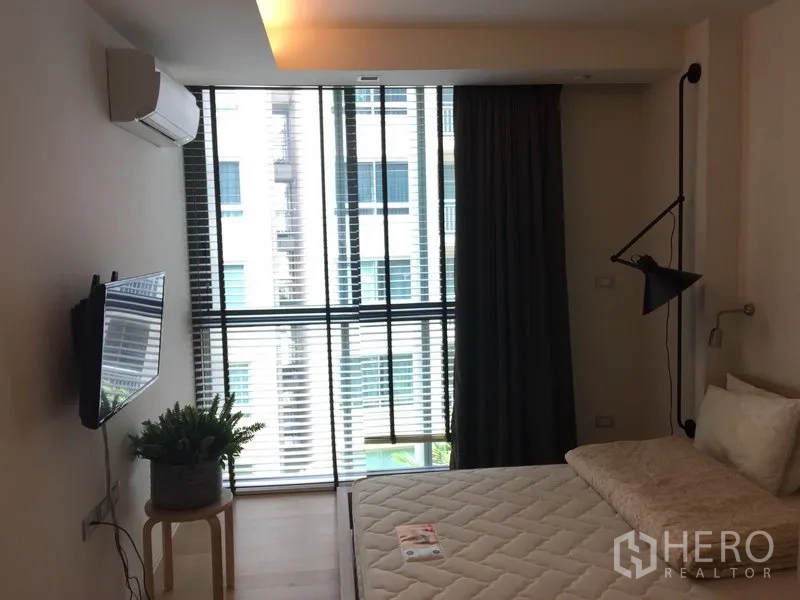 公寓 出租在Watthana, Bangkok - 卧室配落地窗与百叶、壁挂电视以及床侧绿植。