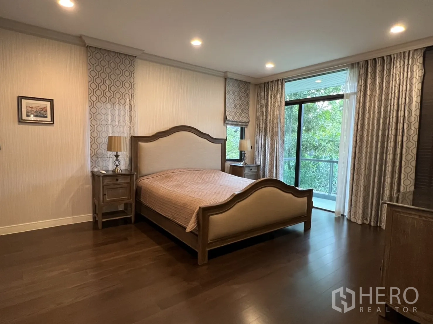 Detached House for rent or sale in Bang Kapi, Bangkok - Master bedroom with wooden floors, king bed and a balcony overlooking greenery.