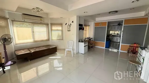 Detached House for sale in Mueang Pathum Thani, Pathum Thani - Bright living room with large windows, glossy tile floors and an open-plan layout leading toward the kitchen.