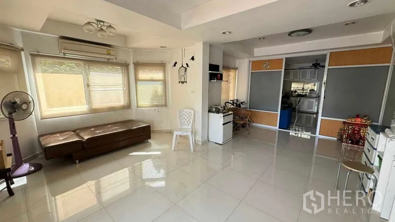Detached House for sale in Mueang Pathum Thani, Pathum Thani - Bright living room with large windows, glossy tile floors and an open-plan layout leading toward the kitchen.
