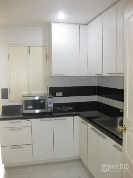 Condominium for rent or sale in Watthana, Bangkok - Compact separate kitchen with white cabinets, black countertops and sink.