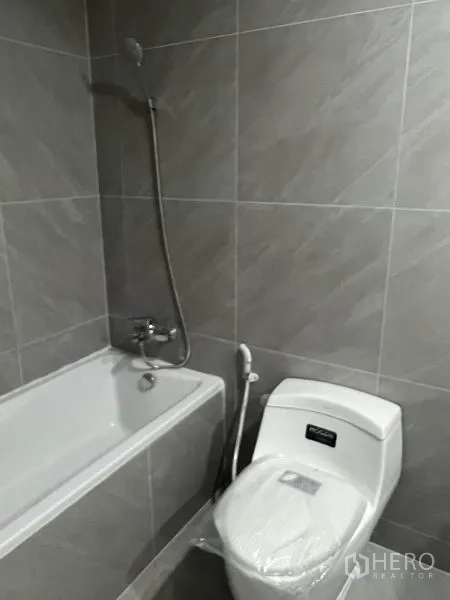 Townhouse for rent in Watthana, Bangkok - Gray-tiled bathroom with bathtub, handheld shower, and toilet.