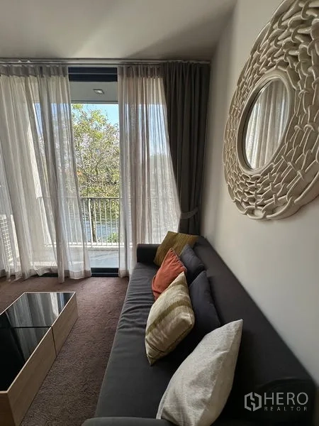 公寓 出租在Watthana, Bangkok - 客厅沙发旁的大落地窗与轻纱帘，圆形装饰镜