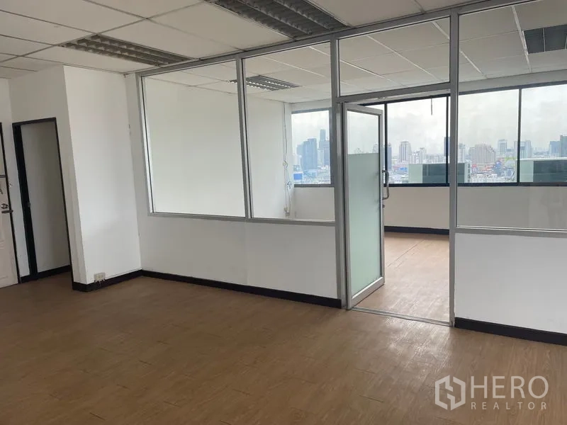 办公空间 出租在Din Daeng, Bangkok - 明亮的办公室内景，玻璃隔间、木纹地板，大窗可观丁登区曼谷天际线。