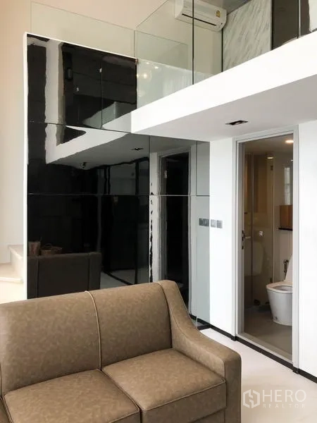 公寓 出租在Sathon, Bangkok - 朝向夹层走道的视角，玻璃墙面与沙发旁的浴室门。
