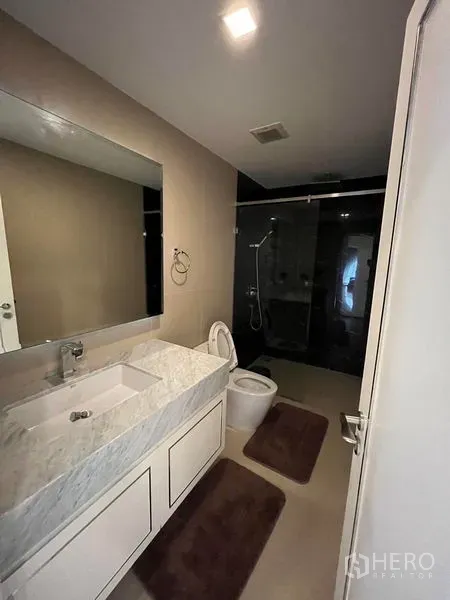 公寓 出售在Bang Rak, Bangkok - 现代浴室，石材洗手台、大镜子与玻璃淋浴间。