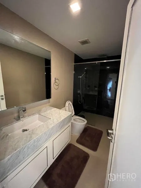 公寓 出售在Bang Rak, Bangkok - 现代浴室，石材洗手台、大镜子与玻璃淋浴间。