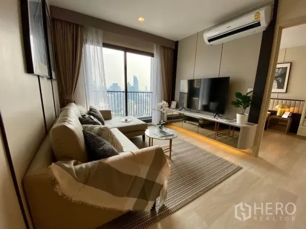 公寓 出租在Pathum Wan, Bangkok - 客厅面向阳台和天际线，带转角沙发、媒体墙，并通往卧室的门。