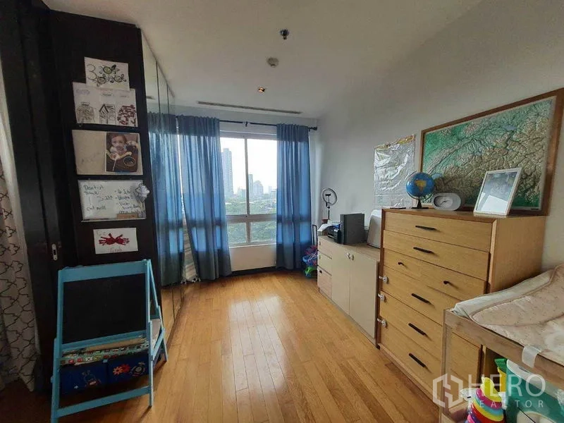 Condominium for rent in Yan Nawa, Bangkok - Bright bedroom or study with blue curtains, dresser and city-view window.