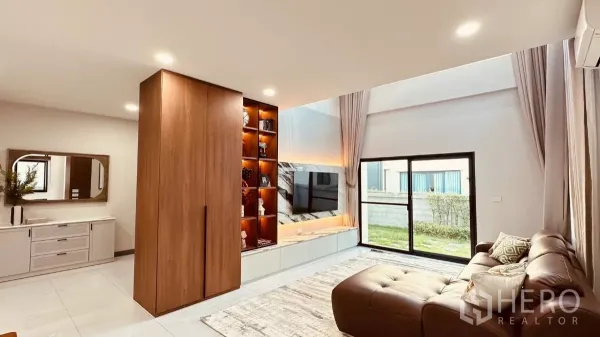 Detached House for rent in Bang Phli, Samut Prakan - Bright living room featuring a marble TV wall, illuminated shelving and large glass doors opening to the lawn.
