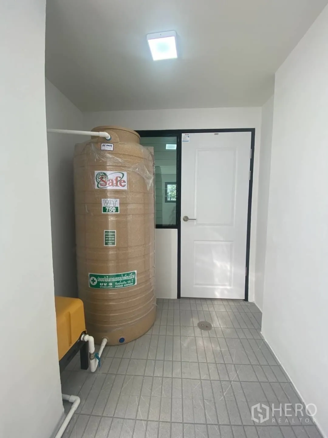 Home Office for sale - Utility area with a 750-liter water tank, tiled floor, and rear access door.