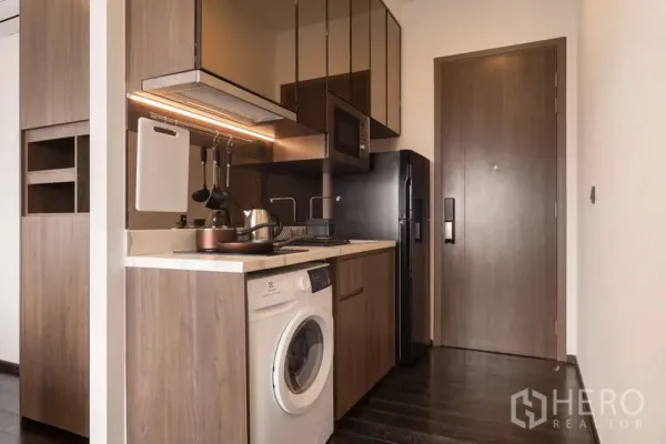 公寓 出租在Watthana, Bangkok - 现代紧凑型厨房，木质柜体、炉灶、微波炉、冰箱和洗衣机