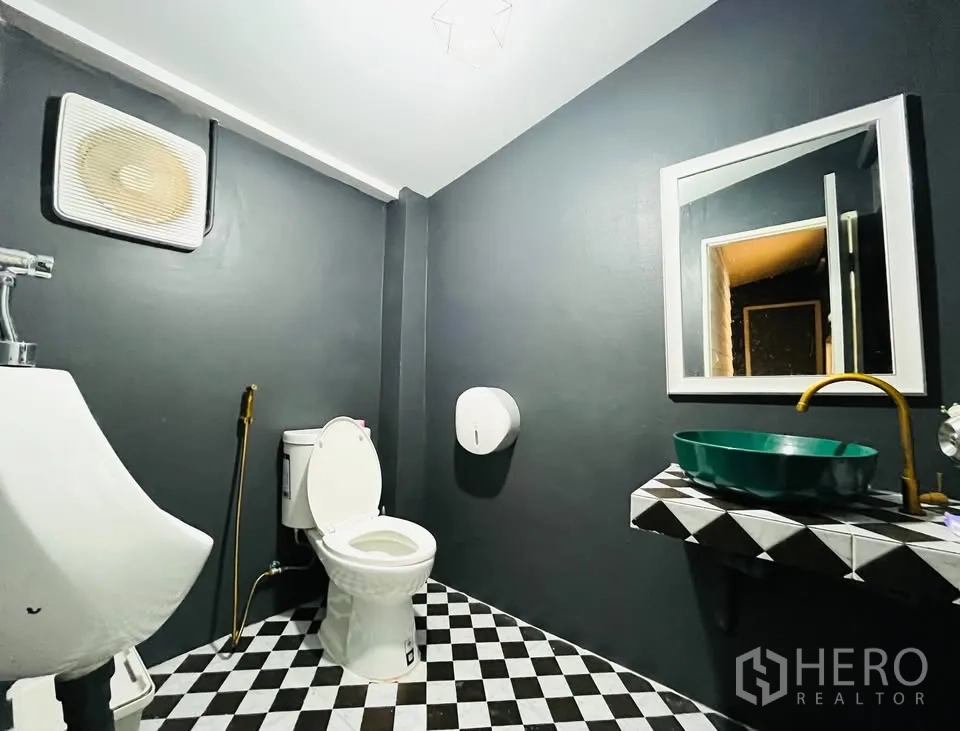 บ้าน ให้เช่า - ห้องน้ำโทนเทา มีโถสุขภัณฑ์ โถปัสสาวะ และอ่างล้างหน้าสีเขียวบนเคาน์เตอร์ลายตาราง
