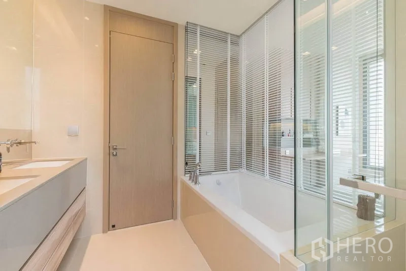 Condominium for rent in Watthana, Bangkok - Spacious bathroom with bathtub, glass partition, double vanity, and neutral finishes.