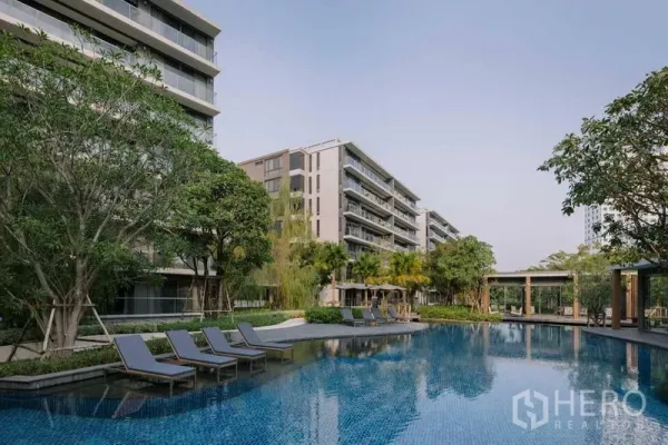 Condominium for sale - Resort-style swimming pool with sun loungers surrounded by low-rise condominium buildings and trees.