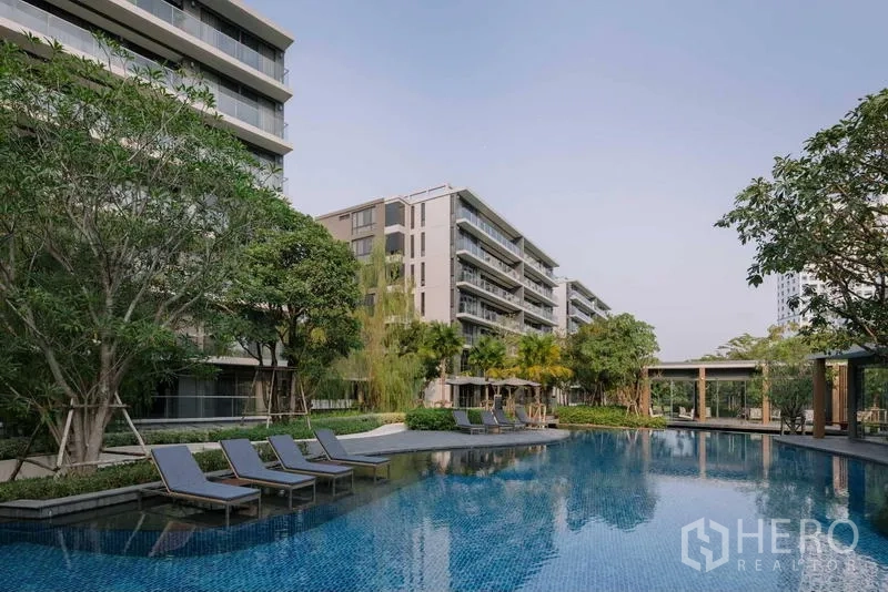 Condominium for sale - Resort-style swimming pool with sun loungers surrounded by low-rise condominium buildings and trees.