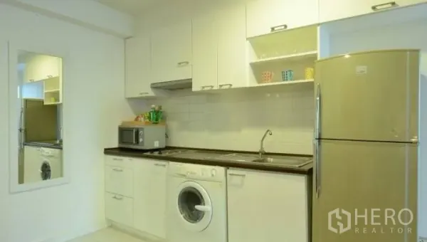 Condominium for rent in Watthana, Bangkok - Modern white kitchen with upper cabinets, sink, microwave, refrigerator and front-loading washing machine.