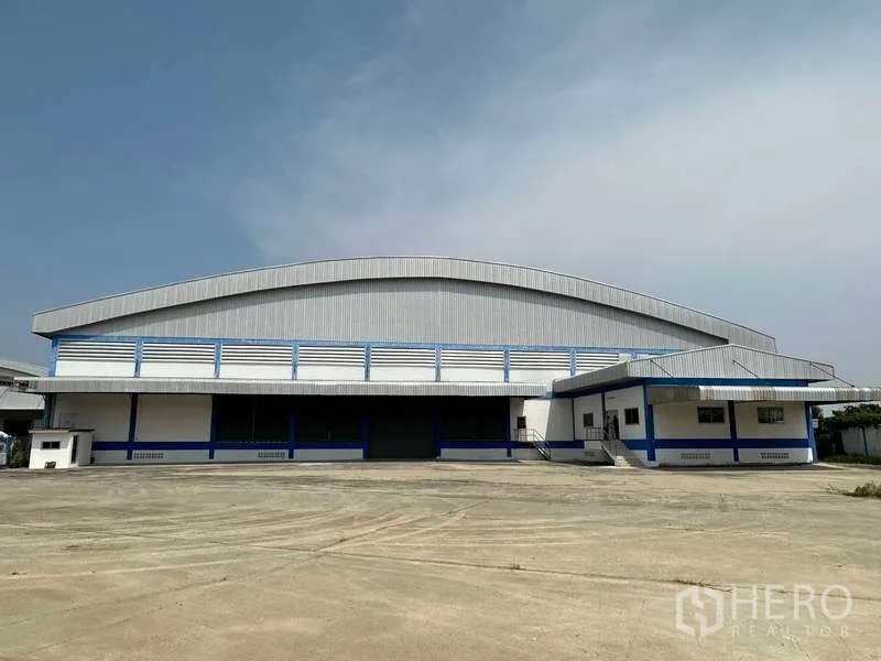 Warehouse for rent in Samut Prakan - Front exterior of a large metal-clad warehouse with attached office and wide concrete yard in Bang Bo.