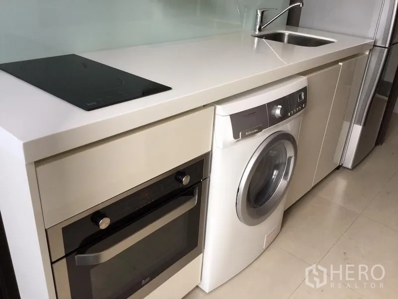 Condominium for rent in Huai Khwang, Bangkok - Compact kitchenette with quartz countertop, induction hob, built-in oven, sink, washing machine and fridge.