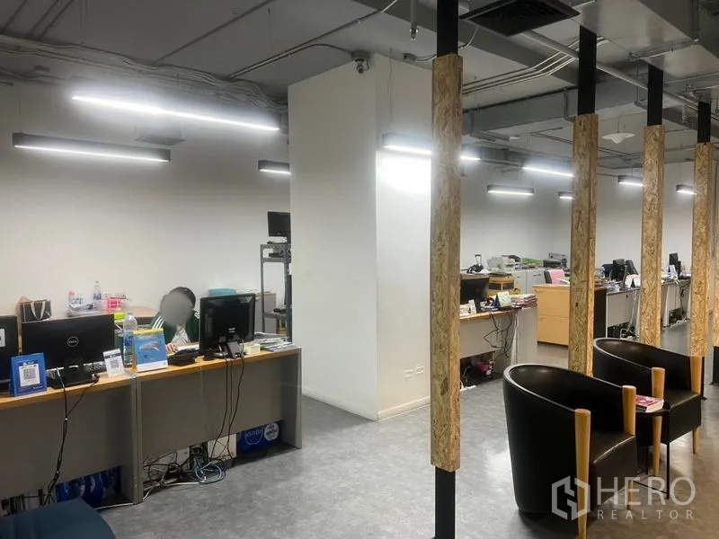Office Space for rent - Row of desks with computers beneath an exposed ceiling, divided by vertical wooden posts in an open office layout.