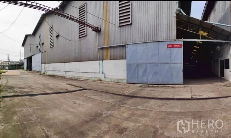 工厂 出租在Krathum Baen, Samut Sakhon - 金属板外墙的大型工厂外观，宽大推拉门与混凝土场地