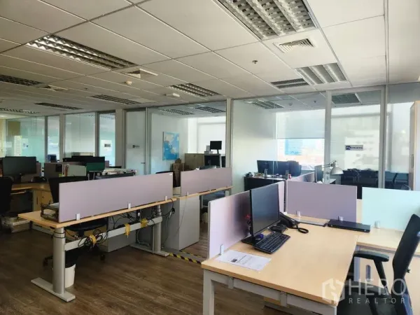Office Space for rent - Open workspace with desks and monitors beside glass-partitioned meeting rooms and ceiling lights.