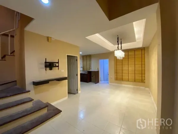 联排别墅 出租在Lat Phrao, Bangkok - 客餐厅一体空间，吊顶、枝形吊灯与旁侧楼梯，采光明亮。