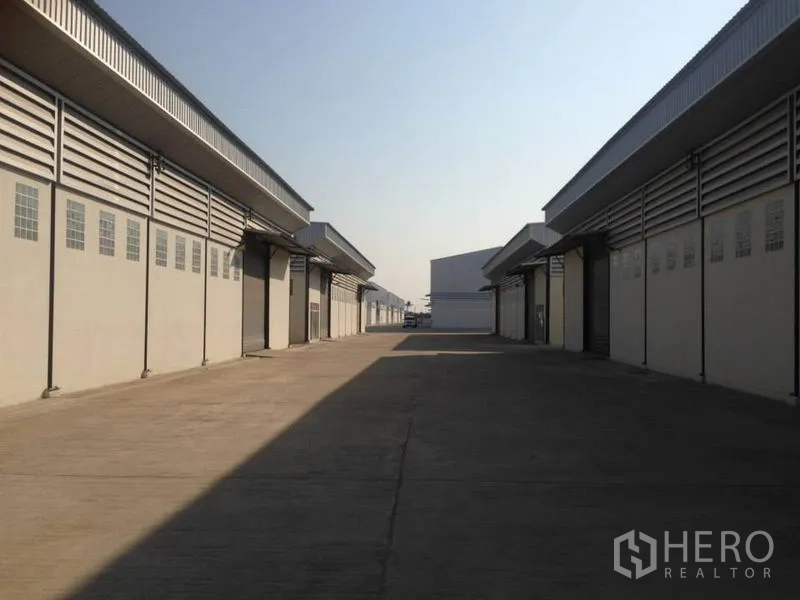 Warehouse for rent in Bang Bua Thong, Nonthaburi - Wide concrete driveway between modern warehouse blocks with roller shutter bays in Bang Bua Thong.