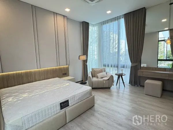 Detached House for rent in Saphan Sung, Bangkok - Spacious bedroom with large bed, armchair, dressing table and tall curtained windows.