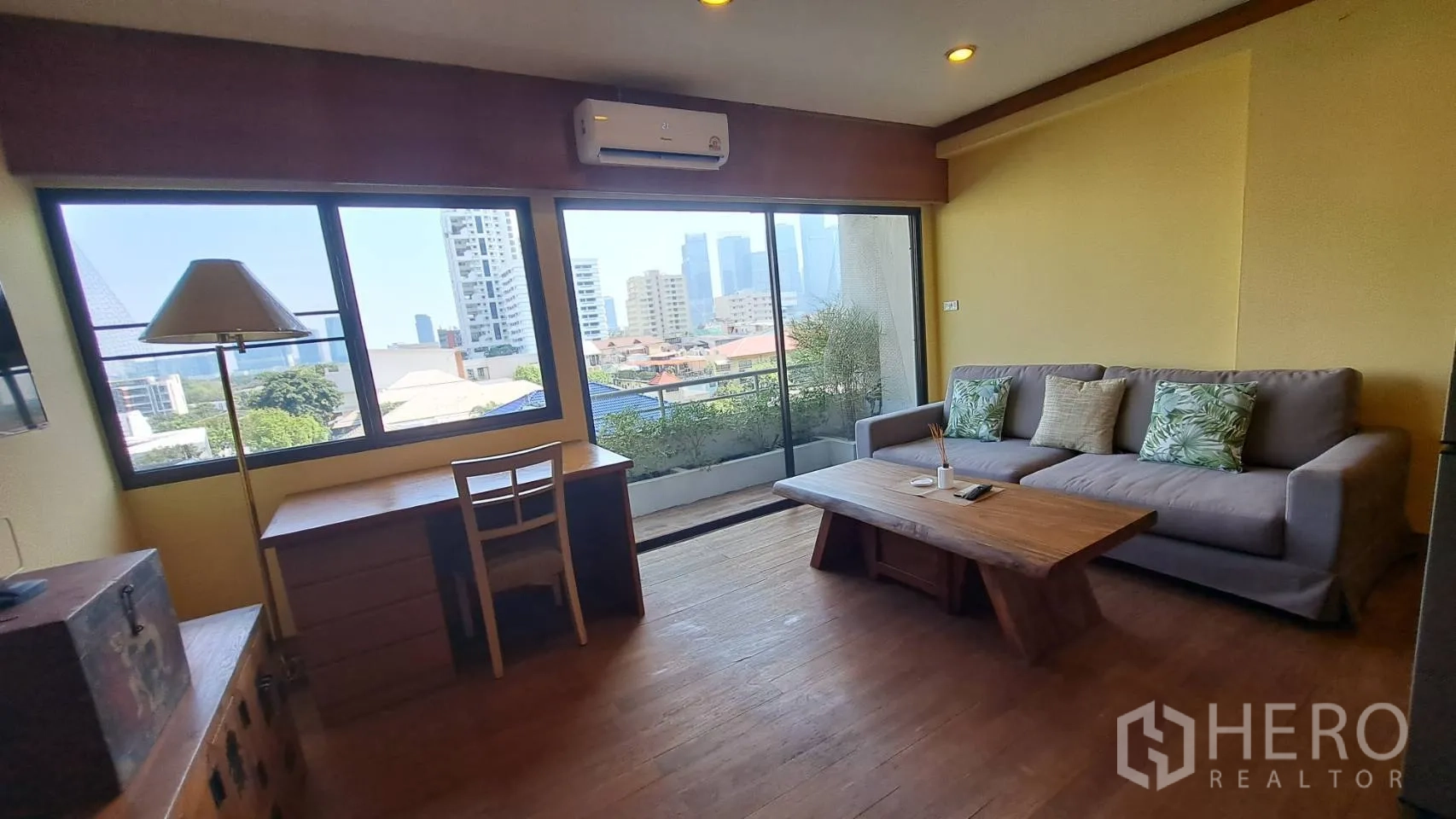 Condominium for rent in Khlong Toei, Bangkok - Bright living room with desk, sofa, and sliding doors to a balcony with skyline view.
