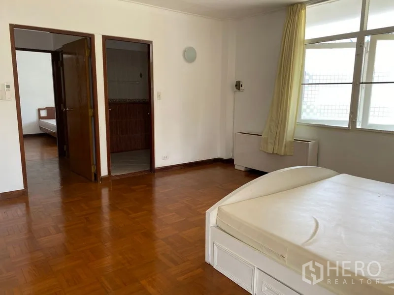 Apartment for rent in Khlong Toei, Bangkok - Master bedroom angle showing entrance to bathroom and second room with parquet floors.