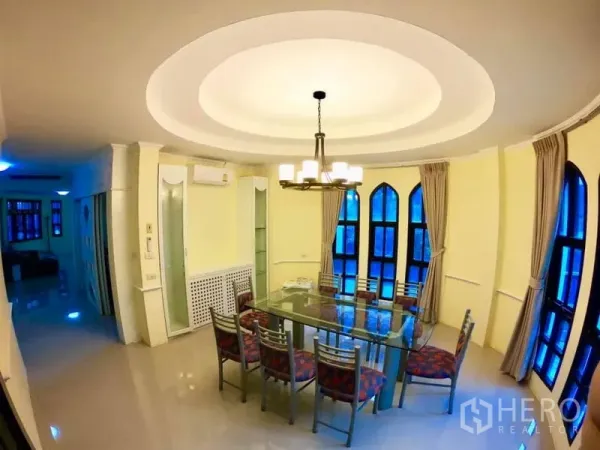 Townhouse for rent in Watthana, Bangkok - Bright dining room with a glass table, eight chairs, chandelier lighting and arched windows with curtains.