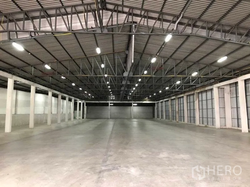 Warehouse for rent in Pak Kret, Nonthaburi - Open warehouse floor showing long spans, smooth concrete surface and rows of loading shutters.