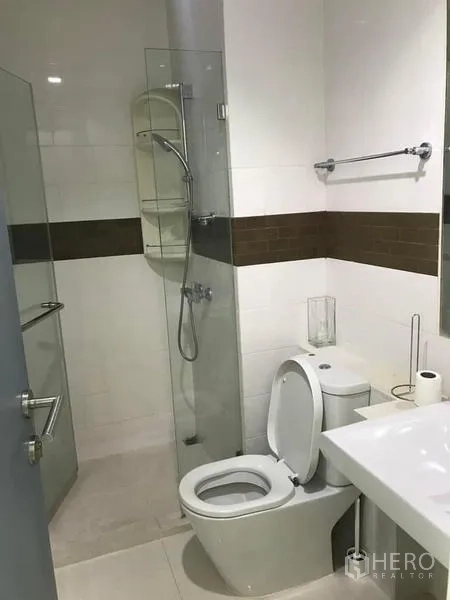Condominium for rent or sale - Bathroom with glass shower, toilet and sleek white tiling.