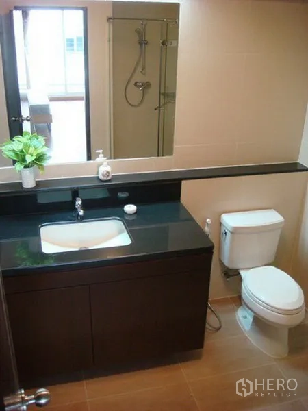Apartment for rent in Khlong Toei, Bangkok - Modern bathroom with dark vanity, basin, toilet and glass-enclosed shower.