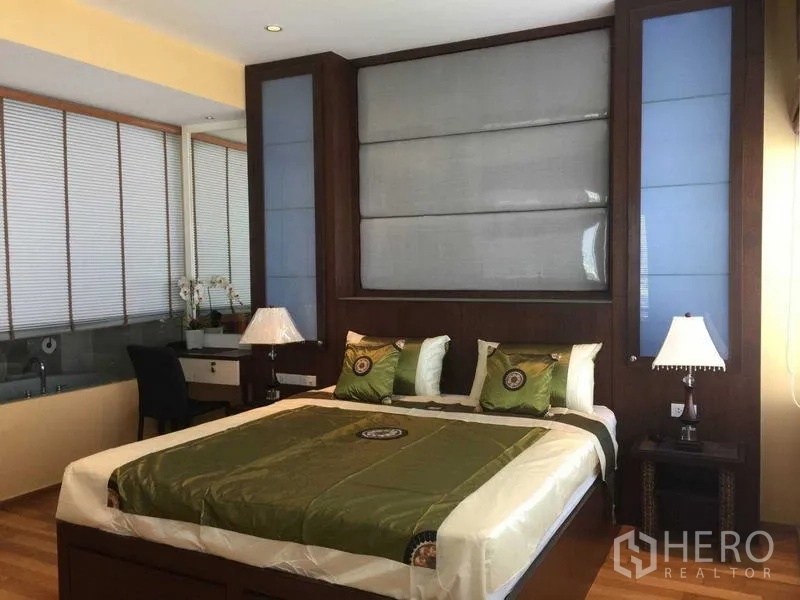 คอนโด ให้เช่า - ห้องนอนผ้าปูสีเขียว โคมไฟหัวเตียง และผนังกระจกเชื่อมต่อห้องน้ำในตัว