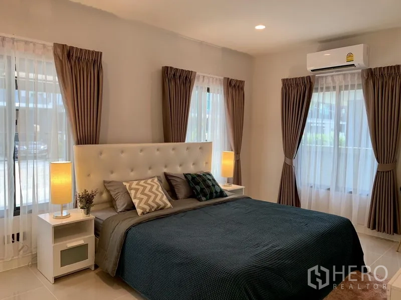Detached House for rent in Bang Kapi, Bangkok - Ground-floor bedroom with white tufted headboard, multiple windows, AC unit and lamps.