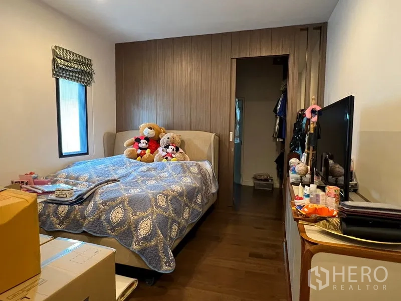 Detached House for sale in Bang Kapi, Bangkok - Cozy bedroom with wood-paneled feature wall, upholstered bed and doorway to a closet.