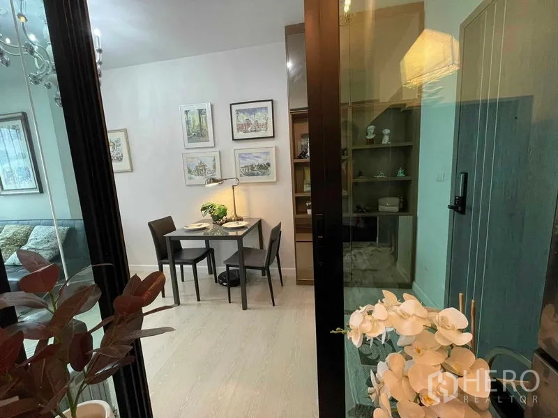 Condominium for sale in Huai Khwang, Bangkok - View through a glass door to the dining area with display shelves and orchid decor.