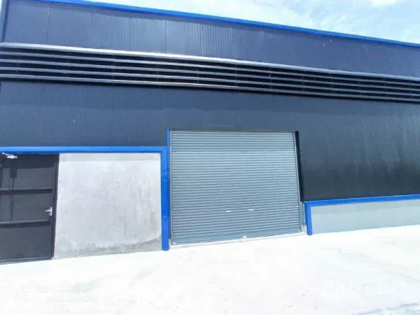 คลังสินค้า ให้เช่าในSaphan Sung, Bangkok - มุมใกล้ของช่องโหลดสินค้า พร้อมประตูม้วนขนาดใหญ่และผนังเมทัลชีทคาดสีน้ำเงิน