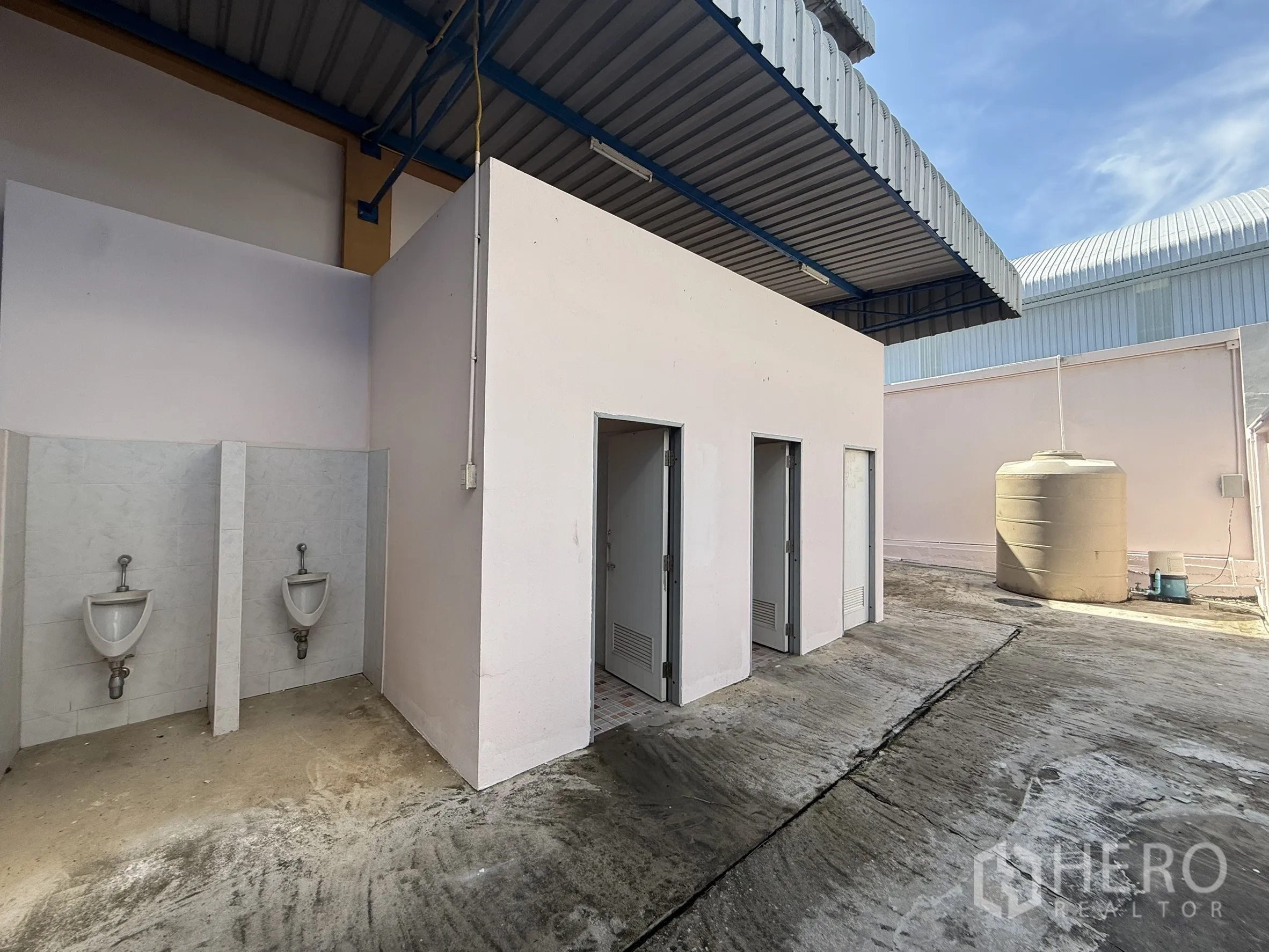 Warehouse for rent or sale in Bang Bo, Samut Prakan - Exterior of restroom block with urinals and additional stalls near water tank.