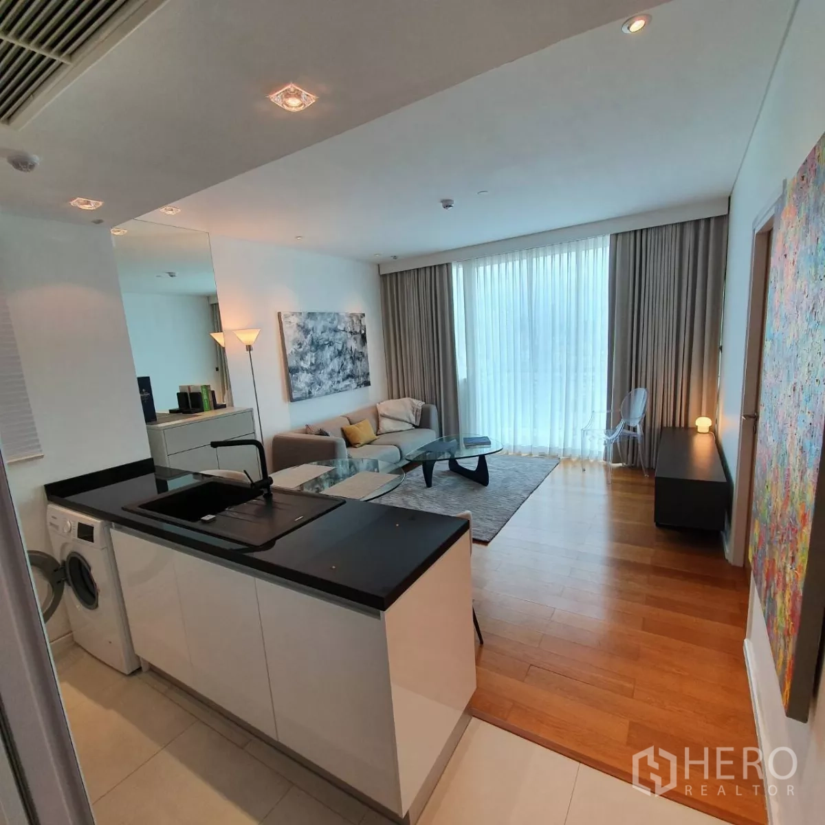 Condominium for rent in Watthana, Bangkok - Open-plan space showing kitchen island with sink, washing machine and floor-to-ceiling curtains.