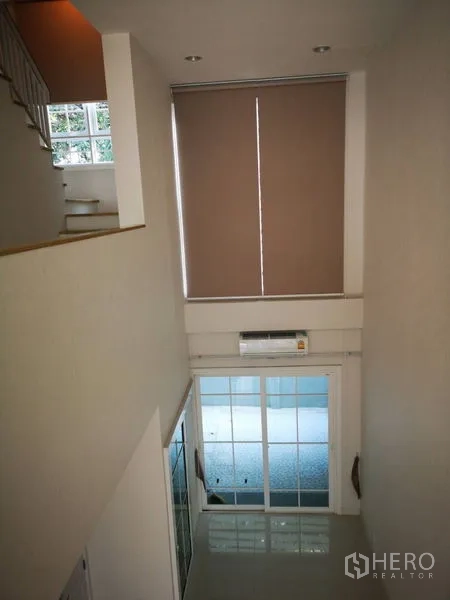 ทาวน์เฮาส์ ให้เช่าในBang Na, Bangkok - มุมมองจากชั้นลอยลงสู่โถงรับแขกเพดานสูงและประตูกระจกบานเลื่อน