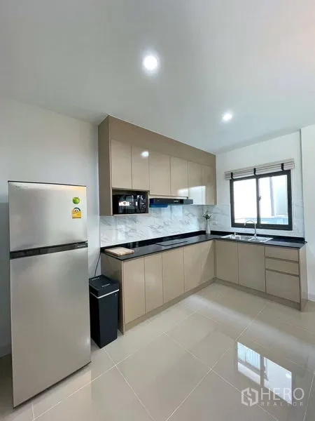 Townhouse for rent in Bang Phli, Samut Prakan - U-shaped kitchen with glossy beige cabinetry, black countertops and stainless fridge.