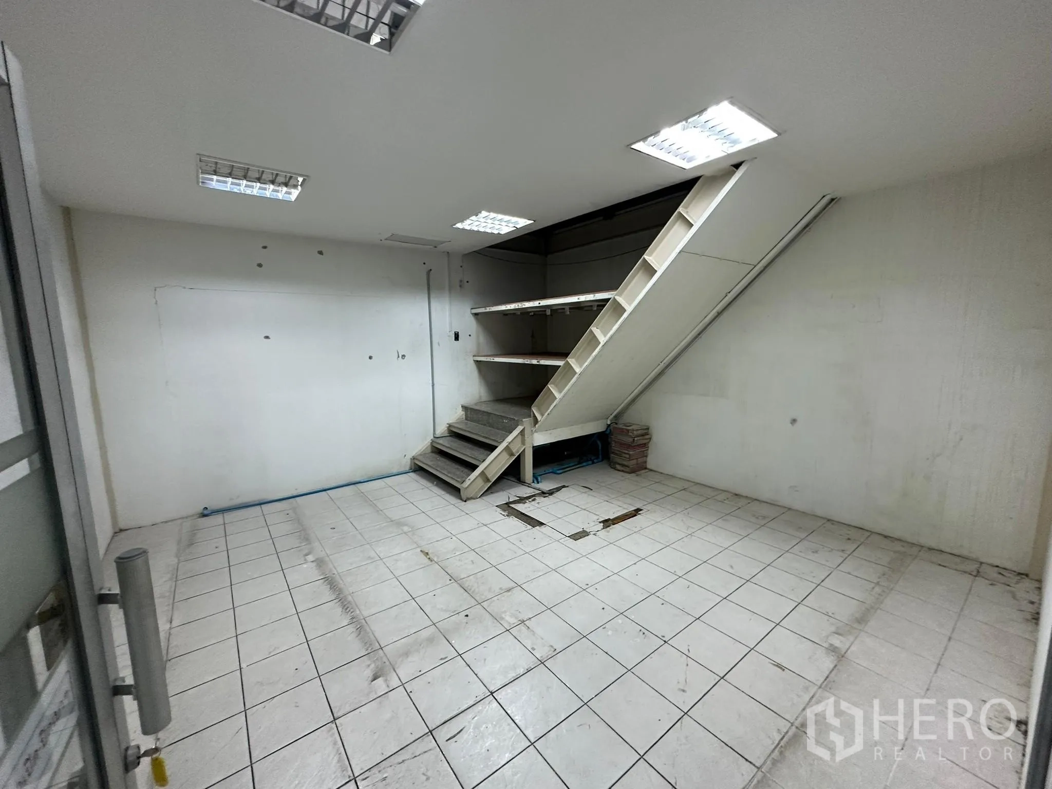 Warehouse for rent in Huai Khwang, Bangkok - Small tiled storeroom with stairs leading to a mezzanine shelf.
