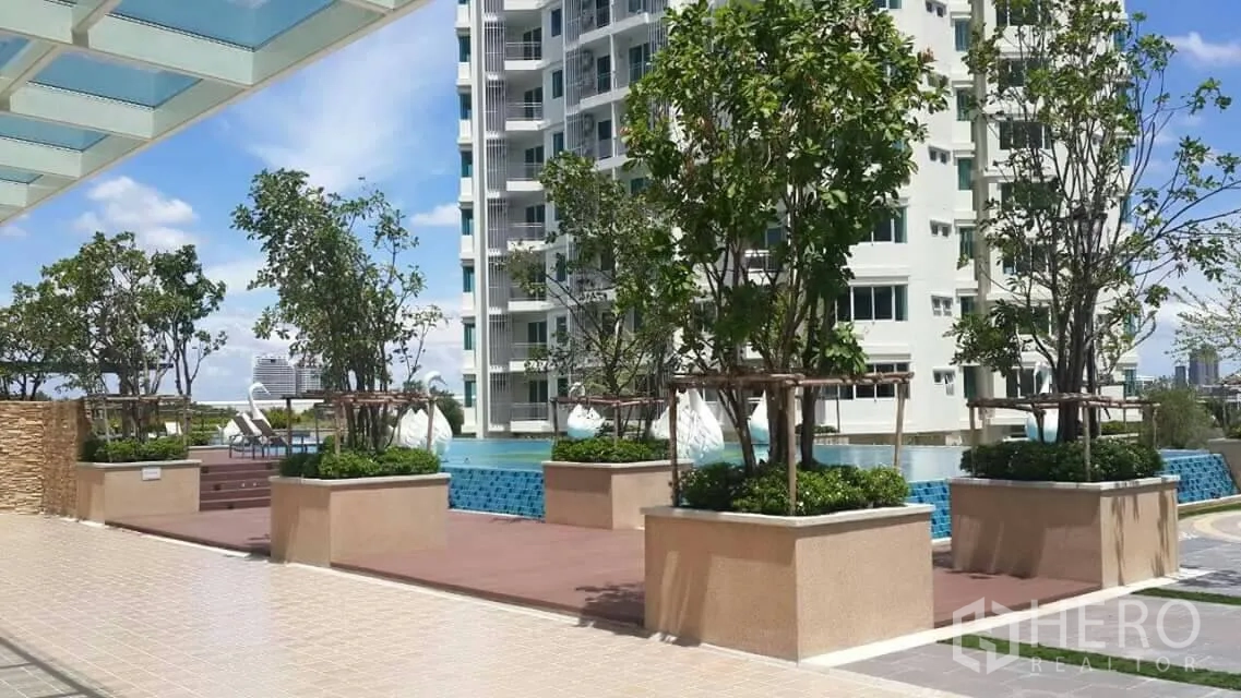 Condominium for sale in Huai Khwang, Bangkok - Landscaped pool deck with planters beside a high-rise condominium under a blue sky.