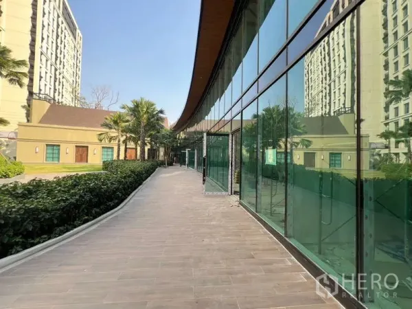 零售空间 出租在Watthana, Bangkok - 绿篱与棕榈树景观步道，旁为绿色玻璃店面