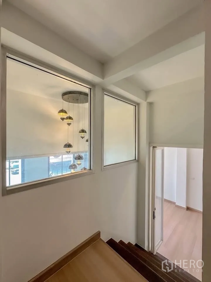 联排别墅 for sale in Wang Thonglang, Bangkok - 楼梯平台设大窗与垂吊灯，俯瞰客厅。