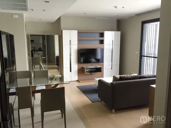 Condominium for rent in Watthana, Bangkok - Open-plan living and dining area with glass table, sofa, built-in TV unit and large window.